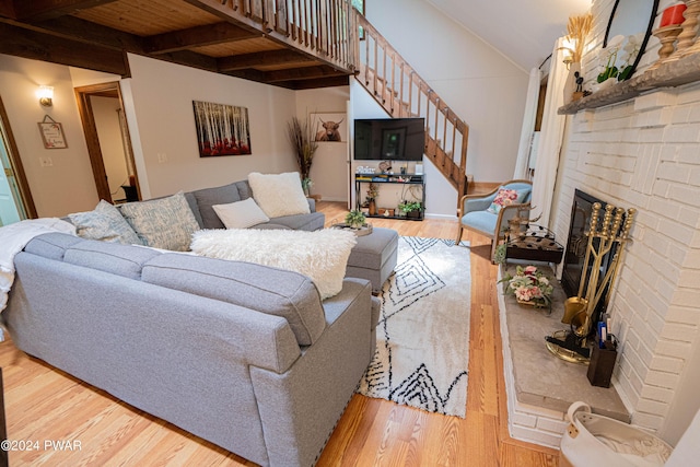 living room with lofted ceiling with beams, light wood-type flooring, wood ceiling, and a brick fireplace