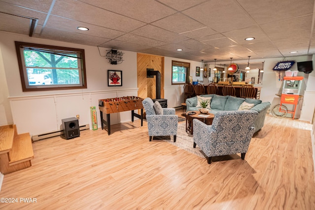 living room with a drop ceiling, a wood stove, baseboard heating, and light hardwood / wood-style flooring