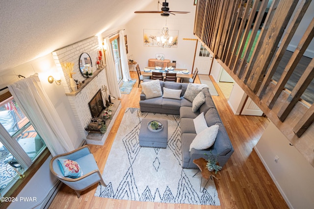 living room featuring a fireplace, a textured ceiling, ceiling fan with notable chandelier, and light hardwood / wood-style flooring