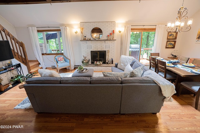 living room with hardwood / wood-style flooring, a brick fireplace, a wealth of natural light, and a notable chandelier