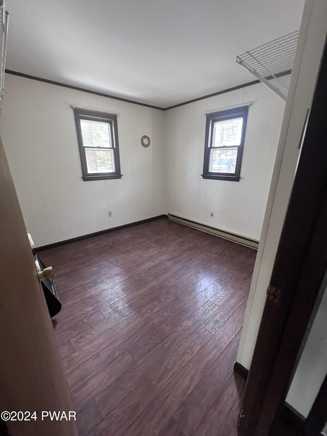 empty room featuring a baseboard heating unit, plenty of natural light, and dark wood-type flooring