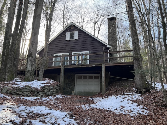 snow covered house with a garage and a wooden deck