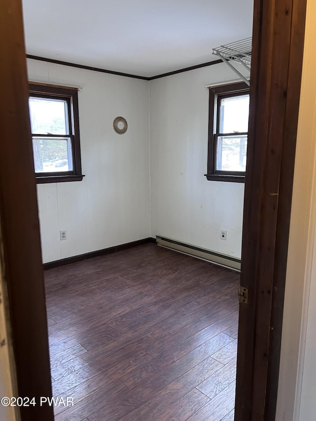 spare room featuring a healthy amount of sunlight, crown molding, baseboard heating, and dark wood-type flooring