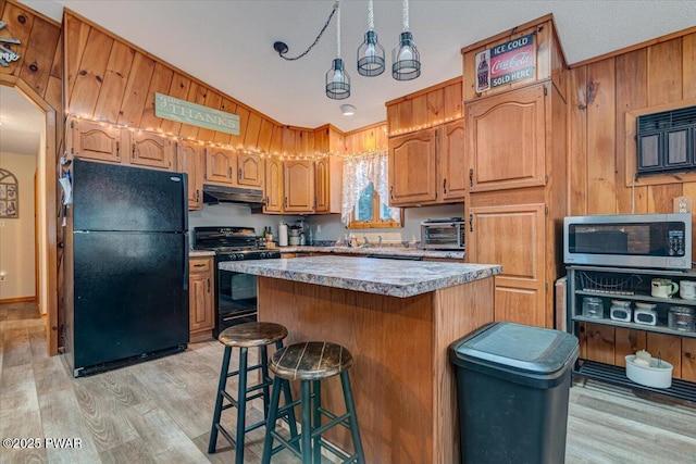 kitchen with black appliances, a kitchen island, a kitchen breakfast bar, wood walls, and light wood-type flooring