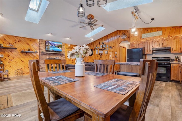 dining room with ceiling fan, light wood-type flooring, lofted ceiling with skylight, and wooden walls