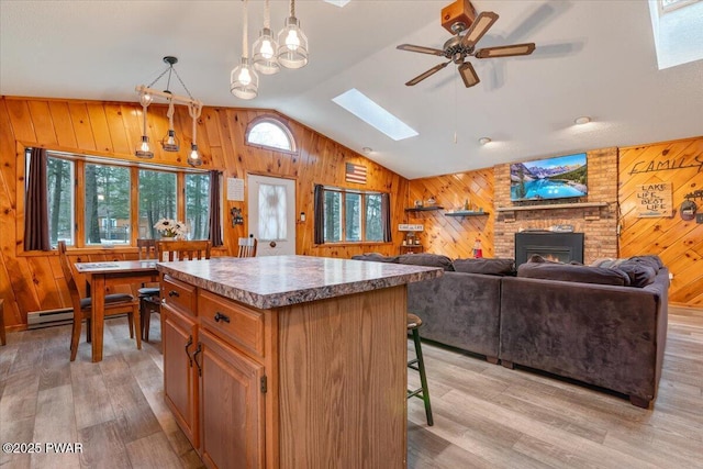 kitchen featuring ceiling fan, decorative light fixtures, light wood-type flooring, vaulted ceiling with skylight, and a center island