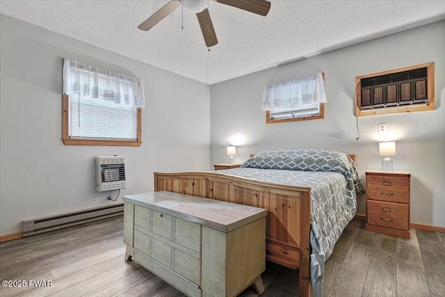 bedroom with ceiling fan, hardwood / wood-style flooring, heating unit, a textured ceiling, and baseboard heating