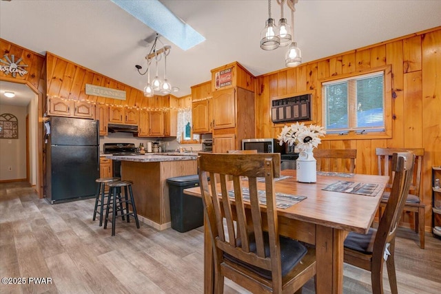 dining room with light wood-type flooring, lofted ceiling with skylight, and wood walls