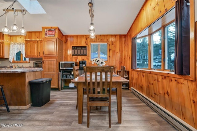 dining area featuring baseboard heating, a skylight, wood walls, and wood-type flooring