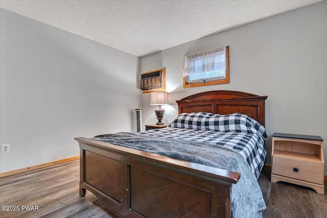 bedroom with wood-type flooring, a textured ceiling, and an AC wall unit