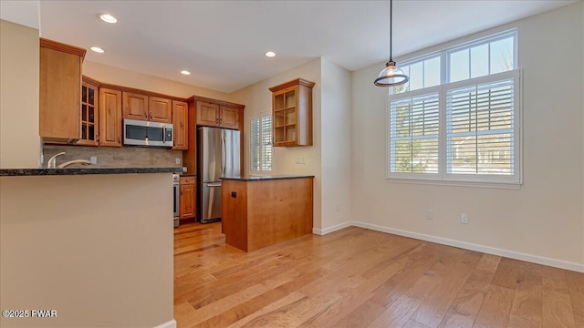 kitchen featuring a peninsula, appliances with stainless steel finishes, light wood-type flooring, brown cabinets, and decorative light fixtures