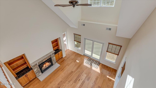 living room with light wood finished floors, a stone fireplace, visible vents, and a healthy amount of sunlight