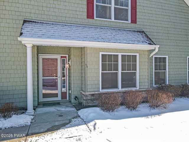 snow covered property entrance featuring roof with shingles