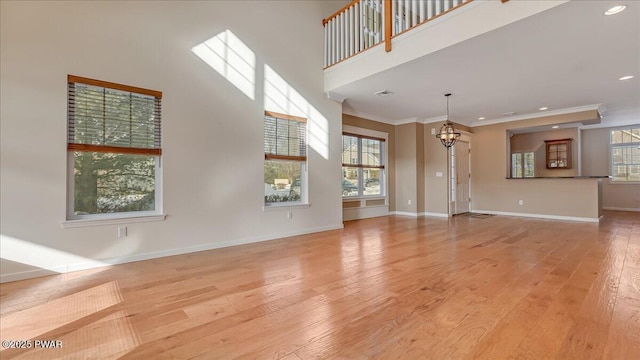 unfurnished living room with a notable chandelier, a towering ceiling, baseboards, ornamental molding, and light wood finished floors