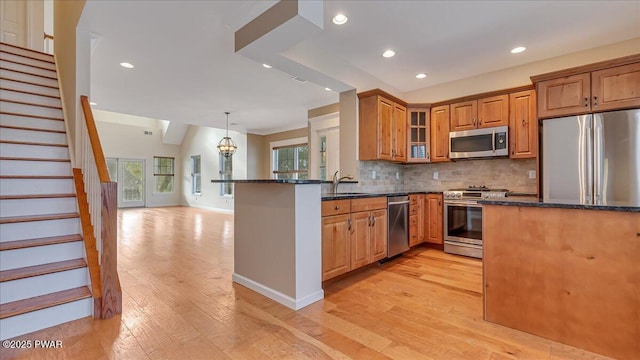 kitchen with pendant lighting, appliances with stainless steel finishes, brown cabinetry, glass insert cabinets, and a peninsula