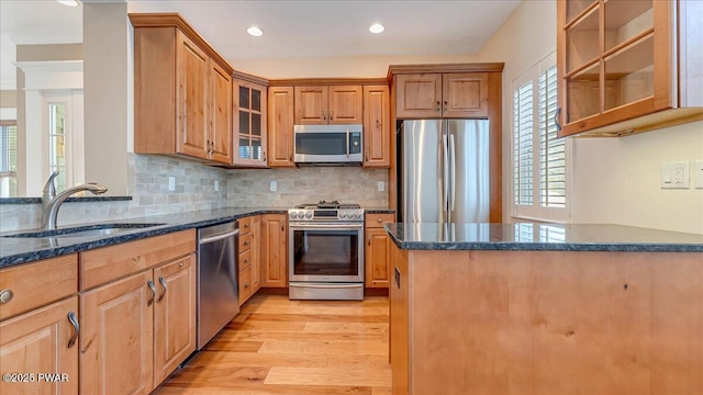 kitchen featuring light wood-style flooring, a sink, appliances with stainless steel finishes, dark stone counters, and glass insert cabinets