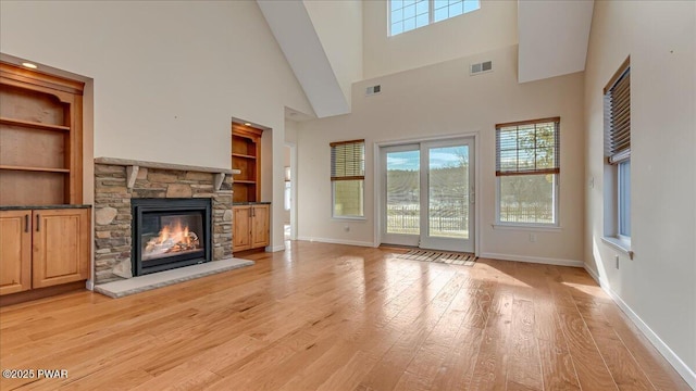 unfurnished living room featuring light wood finished floors, visible vents, and a stone fireplace