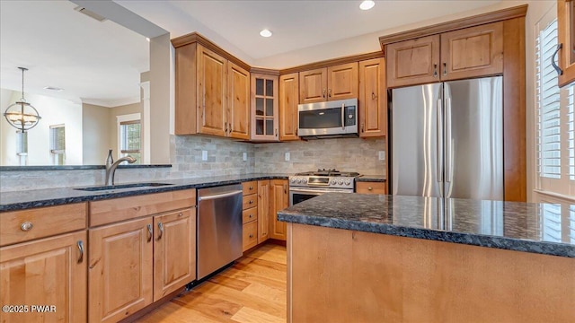 kitchen featuring glass insert cabinets, appliances with stainless steel finishes, dark stone countertops, pendant lighting, and a sink