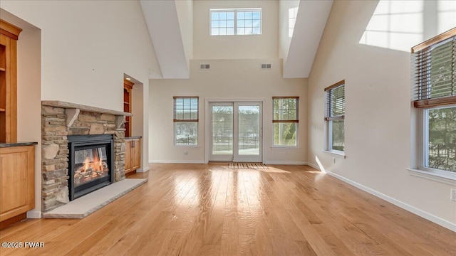 unfurnished living room with light wood-style flooring, visible vents, and a stone fireplace