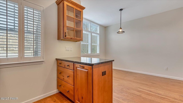 kitchen featuring baseboards, glass insert cabinets, brown cabinets, hanging light fixtures, and light wood-type flooring