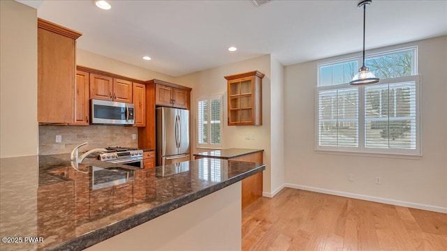 kitchen featuring dark stone counters, appliances with stainless steel finishes, brown cabinets, decorative light fixtures, and a peninsula