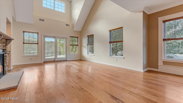 unfurnished living room with light wood-style flooring, a wealth of natural light, visible vents, and a stone fireplace