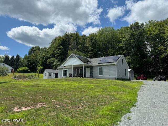 ranch-style home with solar panels, covered porch, and a front yard