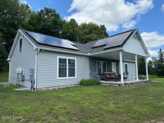 rear view of house with a patio area, a yard, and solar panels