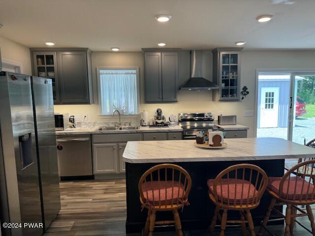 kitchen featuring gray cabinetry, wall chimney exhaust hood, stainless steel appliances, sink, and a center island