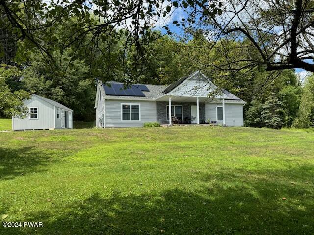 view of front of property featuring a storage shed, a front lawn, a porch, and solar panels