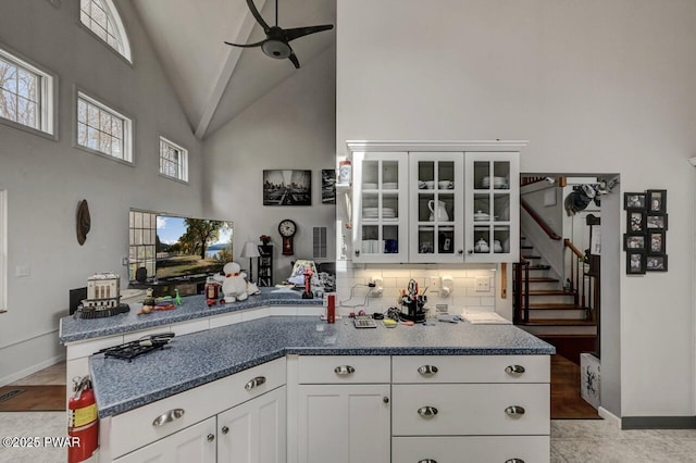 kitchen with glass insert cabinets, backsplash, white cabinets, ceiling fan, and high vaulted ceiling