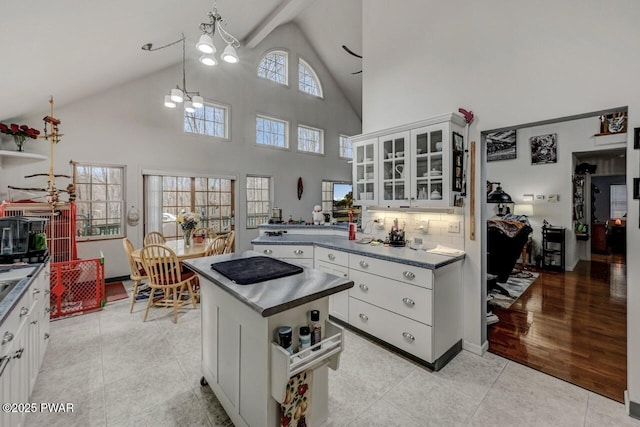 kitchen with light tile patterned floors, glass insert cabinets, white cabinetry, dark countertops, and decorative backsplash