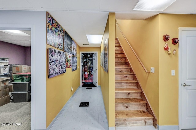 stairway featuring a drop ceiling and baseboards