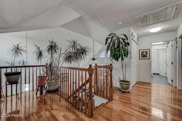 hall featuring wood finished floors, vaulted ceiling, visible vents, and an upstairs landing