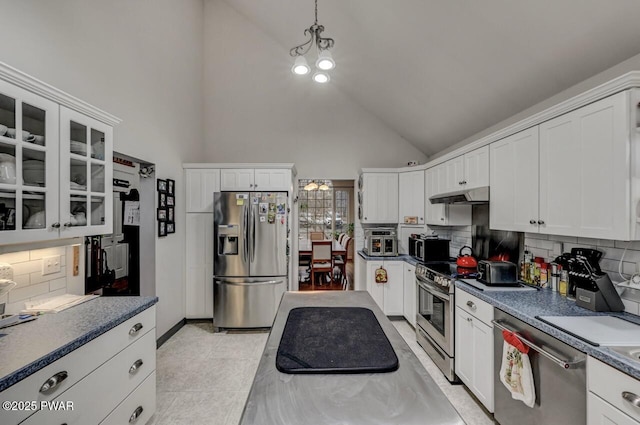 kitchen featuring glass insert cabinets, dark countertops, under cabinet range hood, white cabinetry, and stainless steel appliances