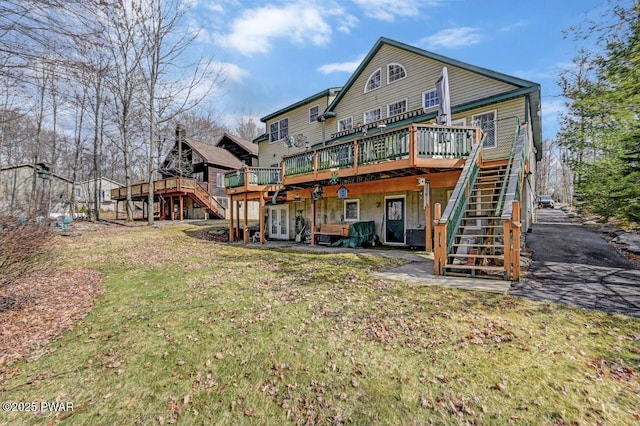 back of house featuring a wooden deck, a patio, a lawn, and stairs