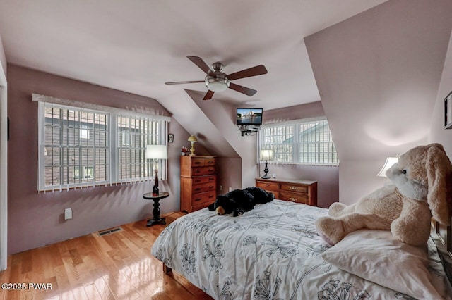 bedroom with light wood-style floors, visible vents, vaulted ceiling, and a ceiling fan
