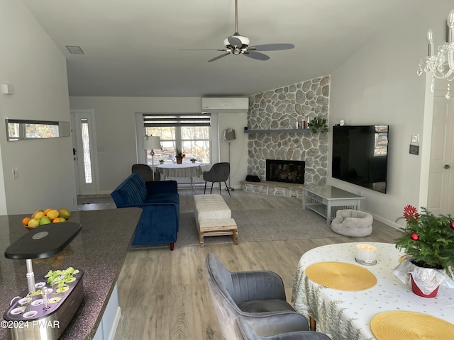 living room featuring ceiling fan, wood-type flooring, an AC wall unit, a stone fireplace, and lofted ceiling