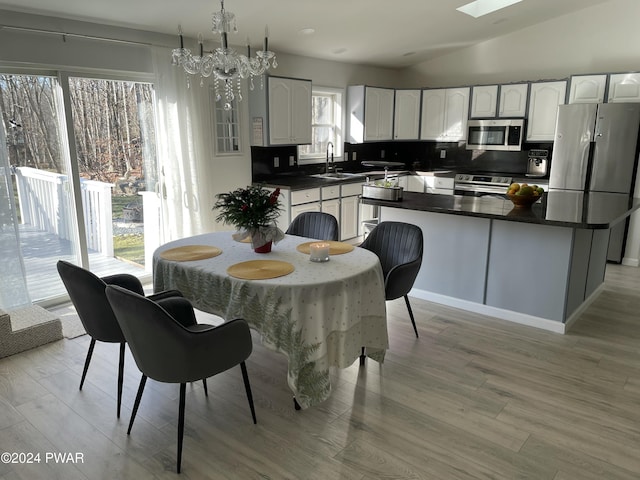 dining room featuring light wood-type flooring, lofted ceiling with skylight, a notable chandelier, and sink