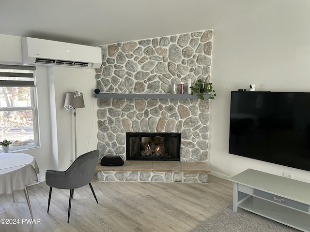 living room featuring a fireplace, light wood-type flooring, and a wall mounted AC