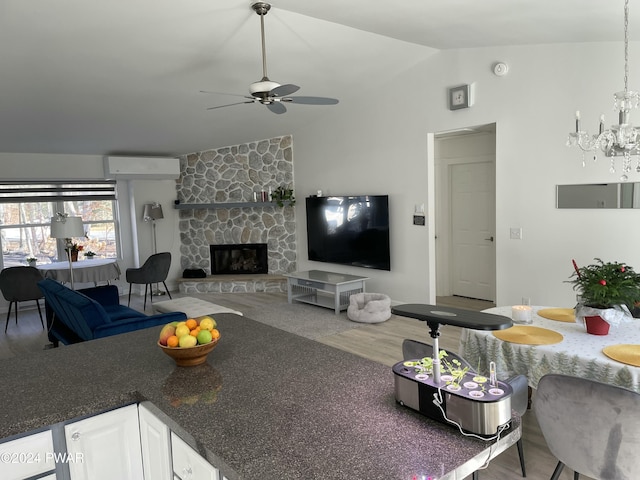 living room featuring a stone fireplace, a wall unit AC, wood-type flooring, lofted ceiling, and ceiling fan with notable chandelier