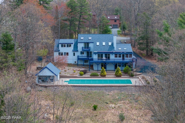 rear view of property featuring a deck, a patio, an outdoor pool, stairs, and a forest view