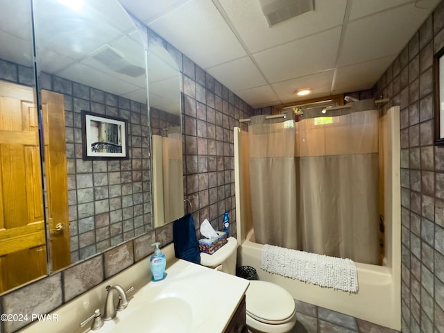 full bathroom featuring toilet, shower / tub combo with curtain, a drop ceiling, and tile walls