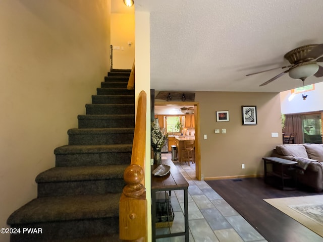 stairs featuring ceiling fan, wood-type flooring, and a textured ceiling