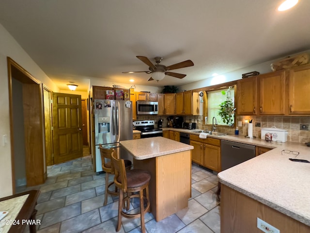 kitchen featuring a kitchen bar, stainless steel appliances, ceiling fan, sink, and a kitchen island