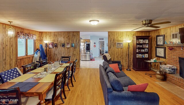 163 Wild Acres Dr, Dingmans Ferry, PA 18328 - dining space with wooden walls, wood finished floors, a ceiling fan, and a brick fireplace