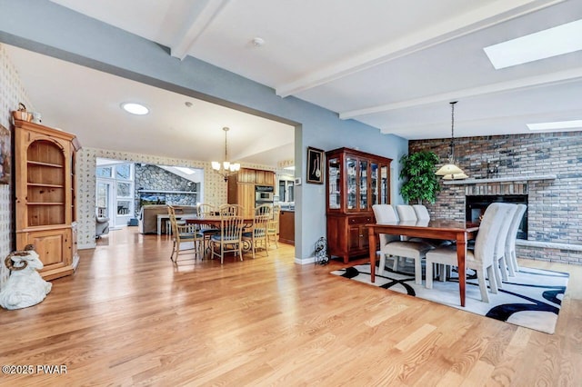 dining space with a skylight, an inviting chandelier, a brick fireplace, light hardwood / wood-style flooring, and beamed ceiling