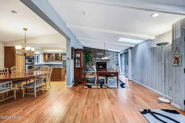 dining room featuring light wood-type flooring, lofted ceiling with skylight, a notable chandelier, a fireplace, and wood walls