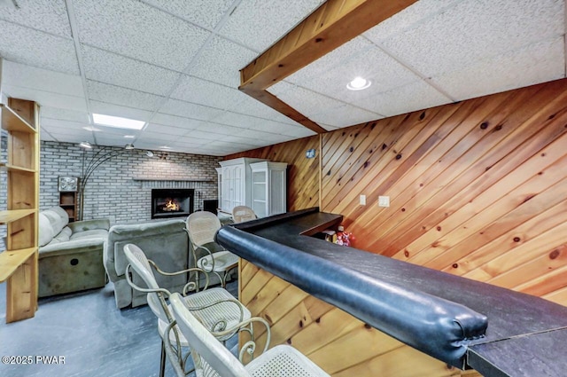 living room with a paneled ceiling, wood walls, and a brick fireplace