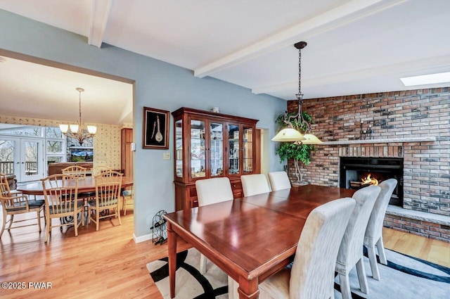 dining room featuring lofted ceiling with beams, french doors, light hardwood / wood-style flooring, and a brick fireplace